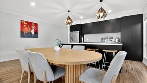 Ein moderner Essbereich mit Holztisch und grau gepolsterten Stühlen, eine Küche mit schwarzen Schränken und Pendelleuchten.