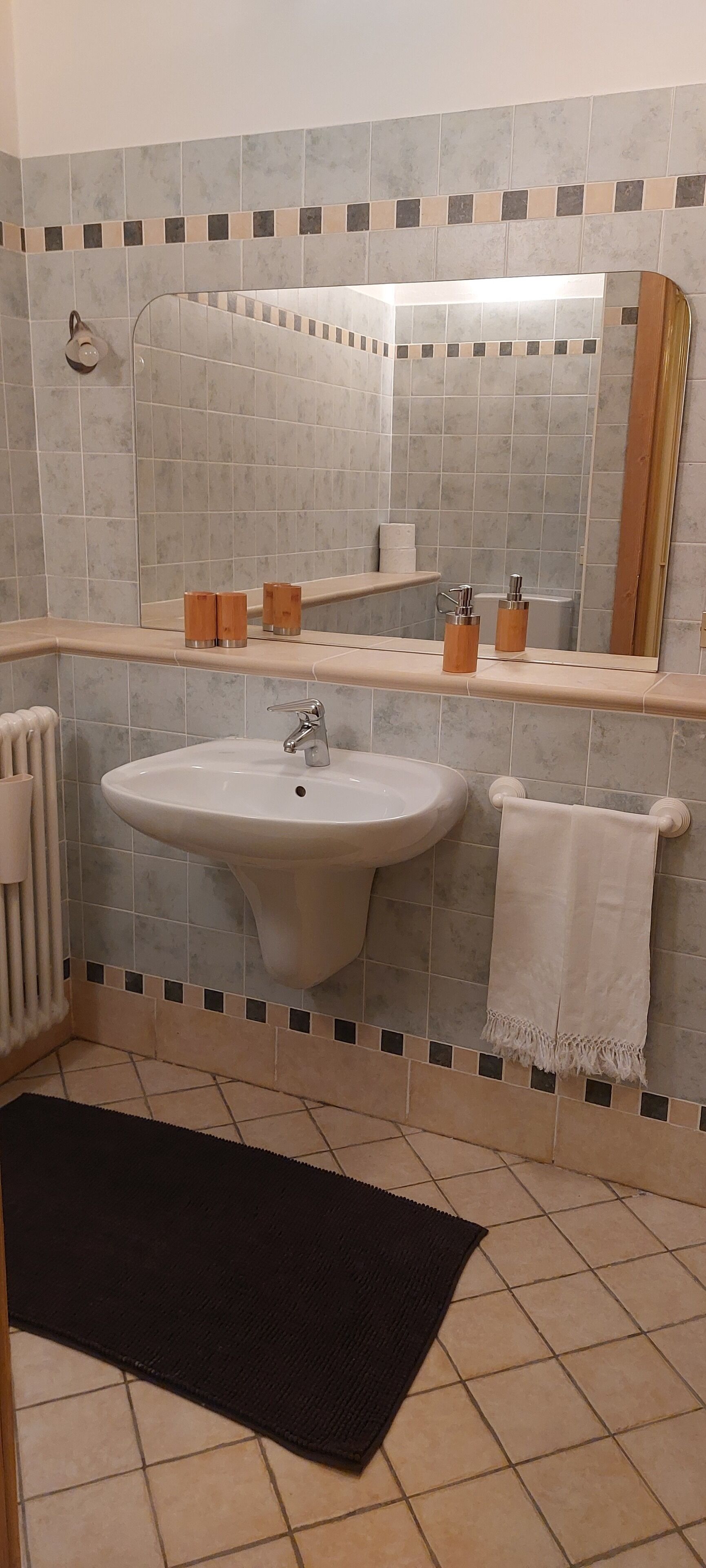 Een badkamer met een wastafel, spiegel, handdoekrek en een zwart vloerkleed.