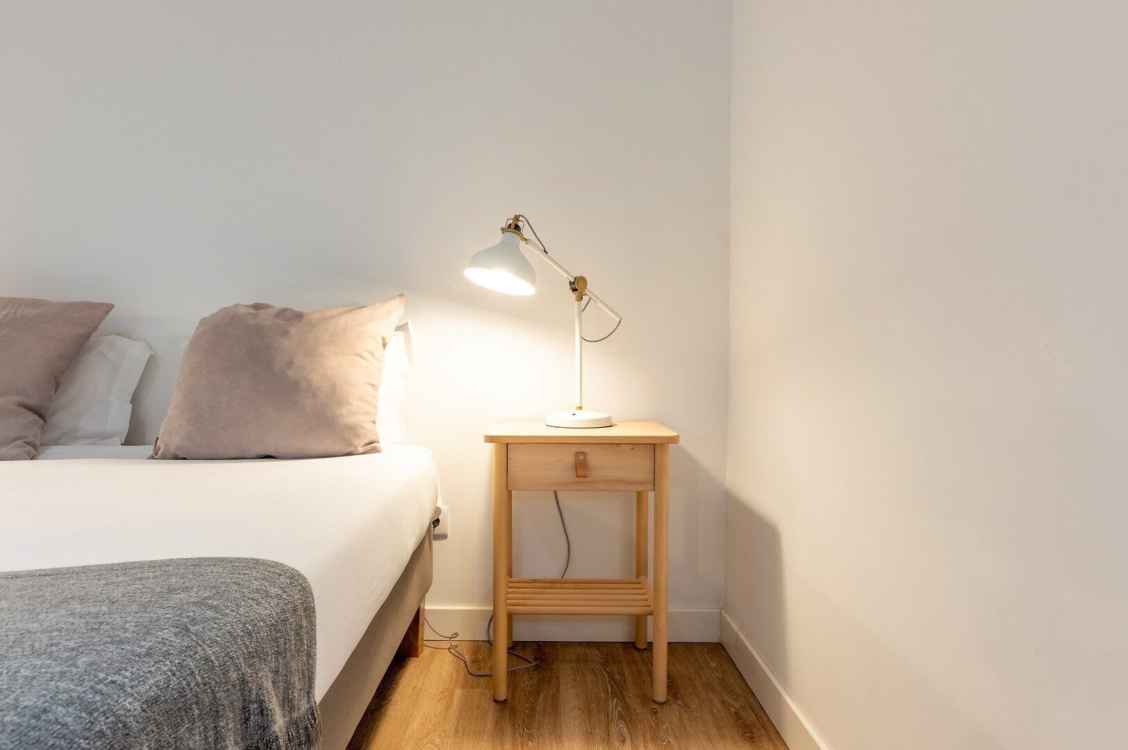 Et soveværelse med en seng, et sengebord, en lampe og et trænatbord.