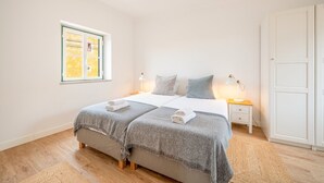 Un dormitorio con cama, mesitas de noche, ventana y puerta.