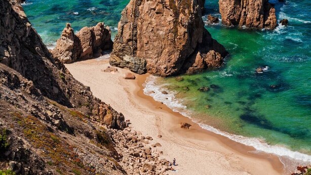 Una costa rocosa con aguas turquesas cristalinas y una playa arenosa.