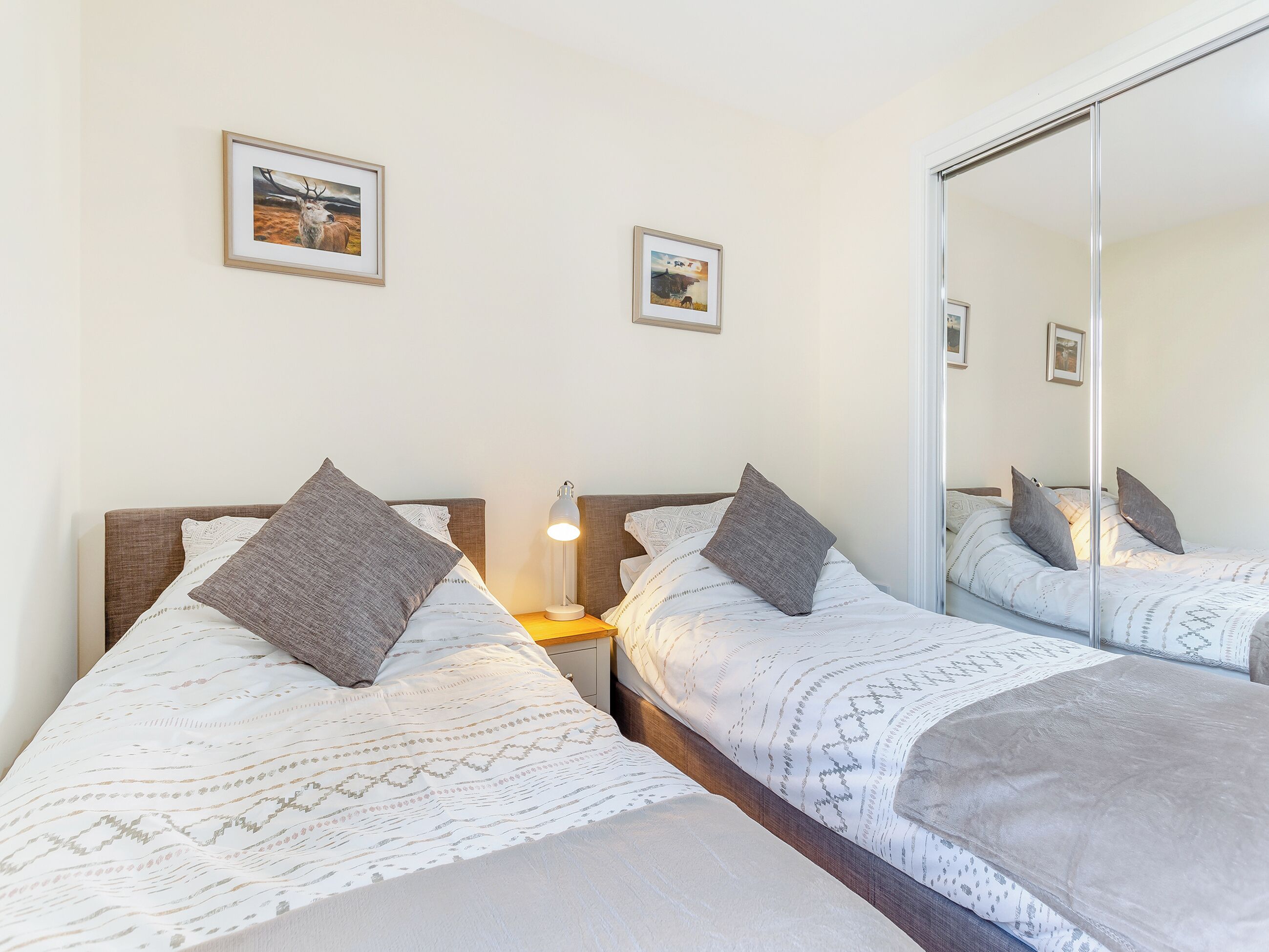 A double bed with patterned bedding and pillows, a bedside lamp, and framed pictures on the wall.