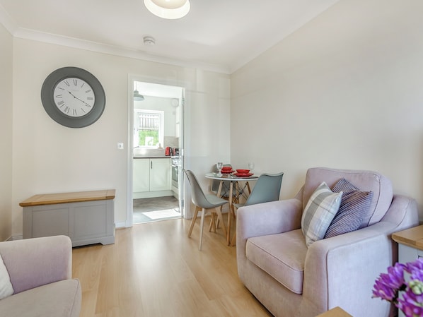 A modern living room with a sofa, a dining table with chairs, and a kitchen in the background.