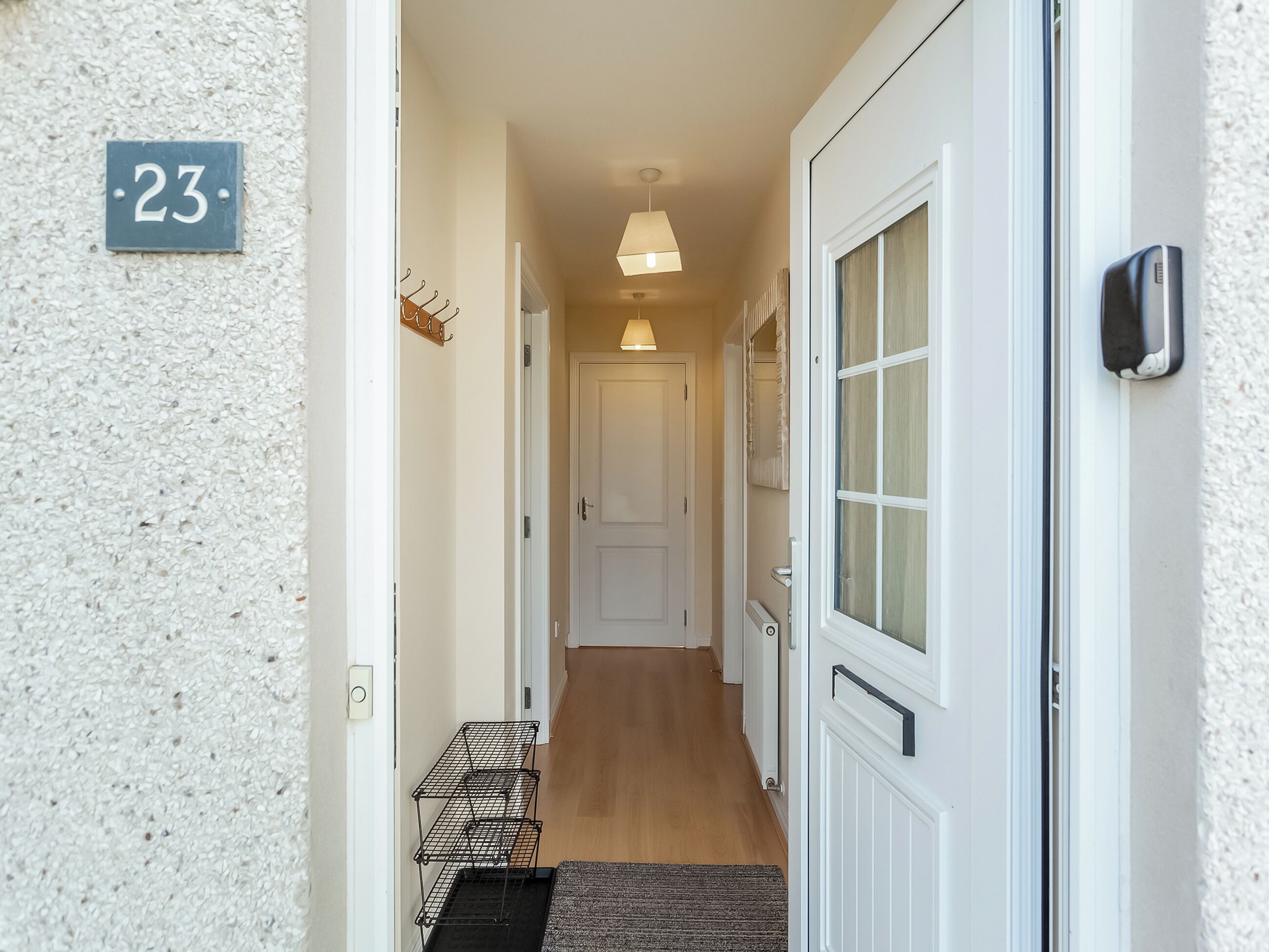 A hallway with a door labeled '23', a hanging light fixture, and a small shelf with items.