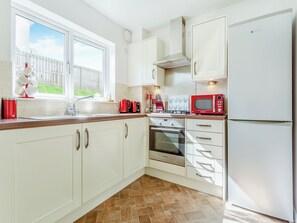 A modern kitchen with white cabinets, a Bosch oven, a red microwave, and a window with a view of a white fence.
