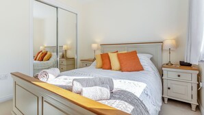Ein Schlafzimmer mit einem großen Spiegel, einem Bett mit vielen Kissen, Nachttischen inklusive Lampen und einem Holz-Kopfstück.