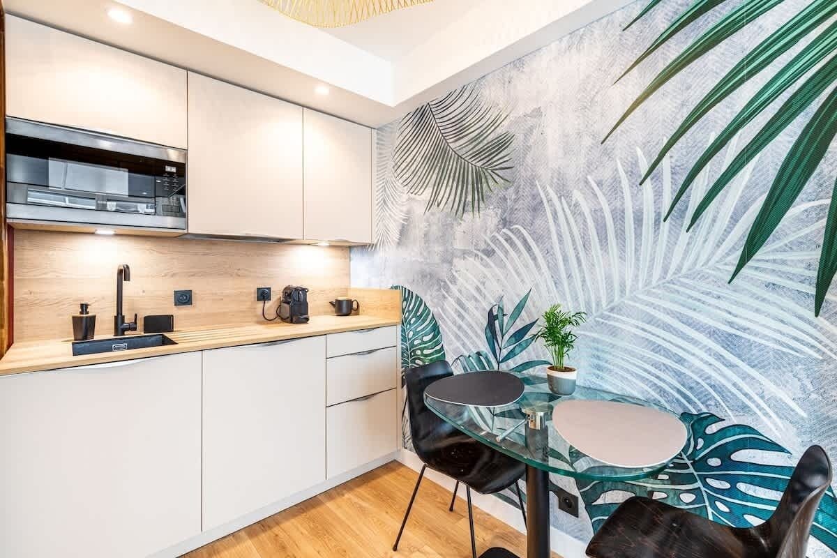 Une cuisine moderne avec des meubles blancs, un plan de travail noir et une table en verre avec des chaises.