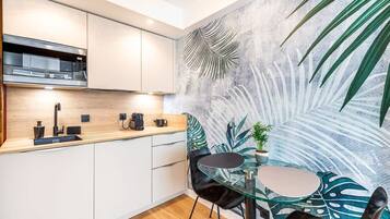 Une cuisine moderne avec des meubles blancs, un plan de travail noir et une table en verre avec des chaises.