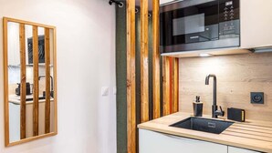 Une cuisine moderne dotée d’un four à micro-ondes encastré, d’un évier avec un robinet noir et de panneaux muraux en bois.