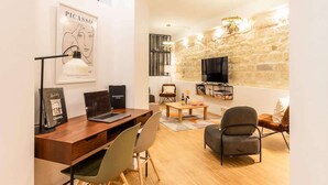 Una sala de estar moderna con una pared de piedra, un televisor de pantalla plana, un escritorio de madera con una computadora portátil, un sofá cómodo y una mesa de centro.
