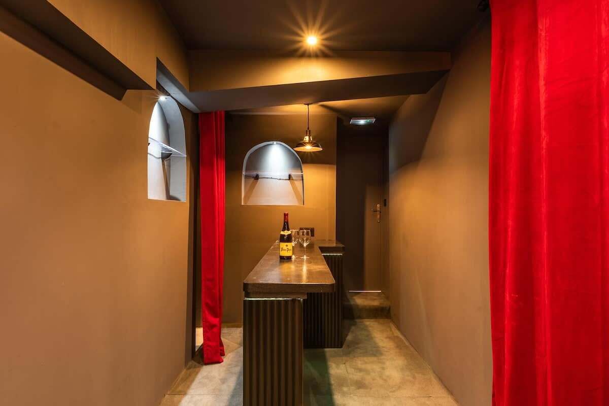 Un couloir étroit avec un coin bar comprenant une bouteille et des verres, un rideau rouge et un luminaire suspendu.