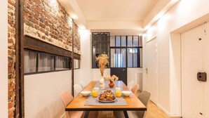 Un comedor con pared de ladrillo, una mesa de madera dispuesta con platos, tazones y un jarrón de flores secas.