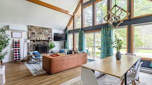 A spacious living room with a fireplace, a dining area, and large windows. - Blue Diamond Hot Tub Fire Pit 3 BDR (Tobyhanna)