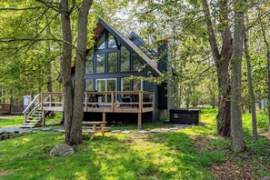 Eine moderne Hütte mit Holzterrasse, großen Fenstern und einer Treppe zu einem Schlafbereich auf dem Dachboden.