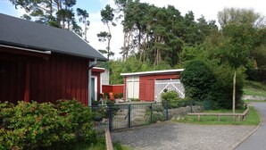 A red building with a white door, a paved driveway, and a fenced area with greenery. - Holiday Home 'Waren An Der Müritz' with Lake View, Private Terrace and Wi-Fi (Waren (Müritz))
