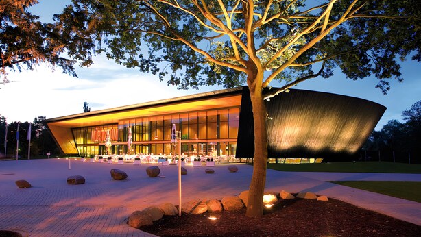 A modern building with a curved facade, a tree in the foreground, and a paved area with rocks. - Holiday Home 'Waren An Der Müritz' with Lake View, Private Terrace and Wi-Fi (Waren (Müritz))