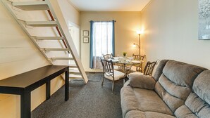 A cozy living room with a sofa, a dining table with chairs, a staircase, and a window with curtains. - Walk to Dtwn Seneca Falls: Family Retreat w/ Yard! (Seneca Falls)