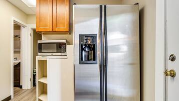 A stainless steel refrigerator with a water dispenser, a microwave, and wooden cabinets above it.