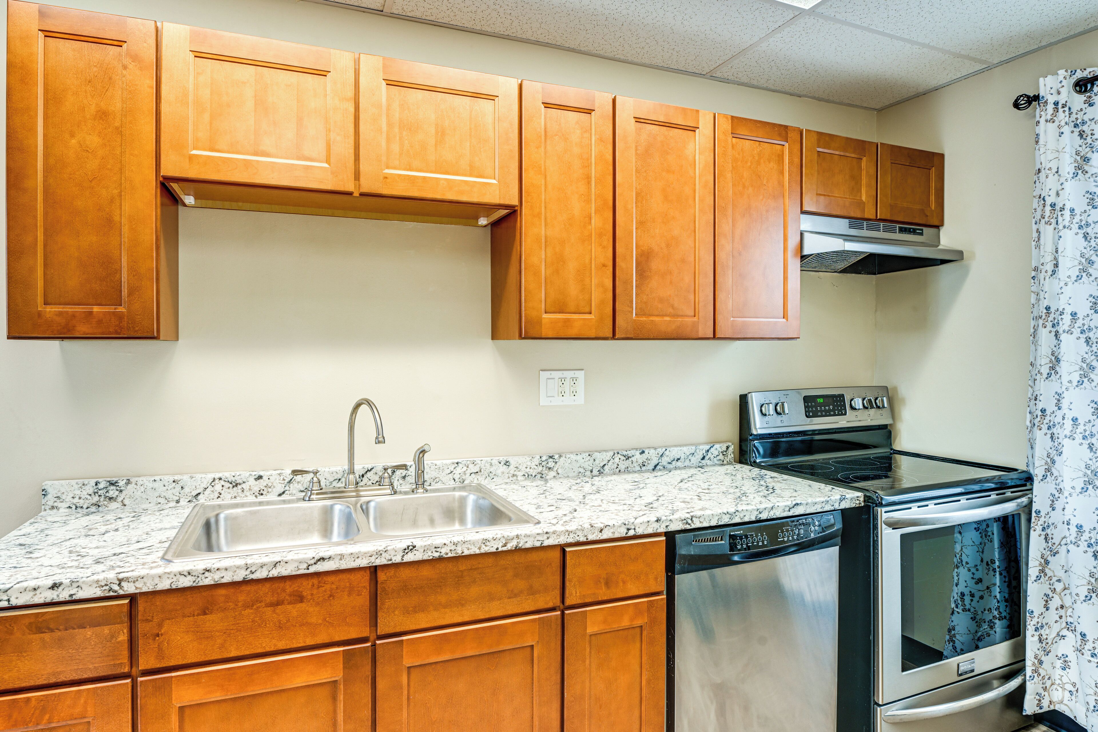 A kitchen with wooden cabinets, a stainless steel sink, a dishwasher, and an oven.