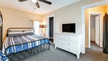 A bedroom with a bed, a TV on a dresser, a ceiling fan, and a door leading to another room.
