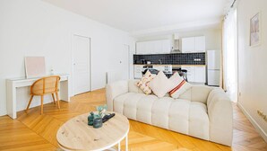 Una sala de estar moderna con un sofá, una mesa redonda de centro y un área de comedor con una silla y una pequeña mesa.