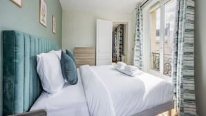 Habitación de hotel con cama, cabecera, armario, puerta y ventana con cortinas.