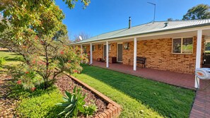 A brick building with a covered porch, a lawn, and a garden with flowering plants.