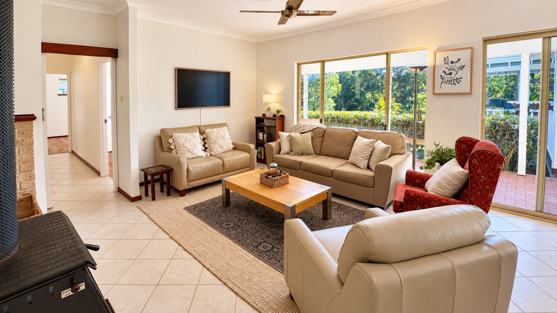 A living room with a sofa set, a coffee table, and a TV. There is a window with a view of greenery outside.
