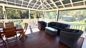 Un patio techado al aire libre con mobiliario de madera, incluyendo una mesa y sillas, y un sofá.