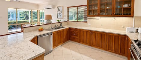 A modern kitchen with wooden cabinets, a built-in dishwasher, and a large window providing natural light.
