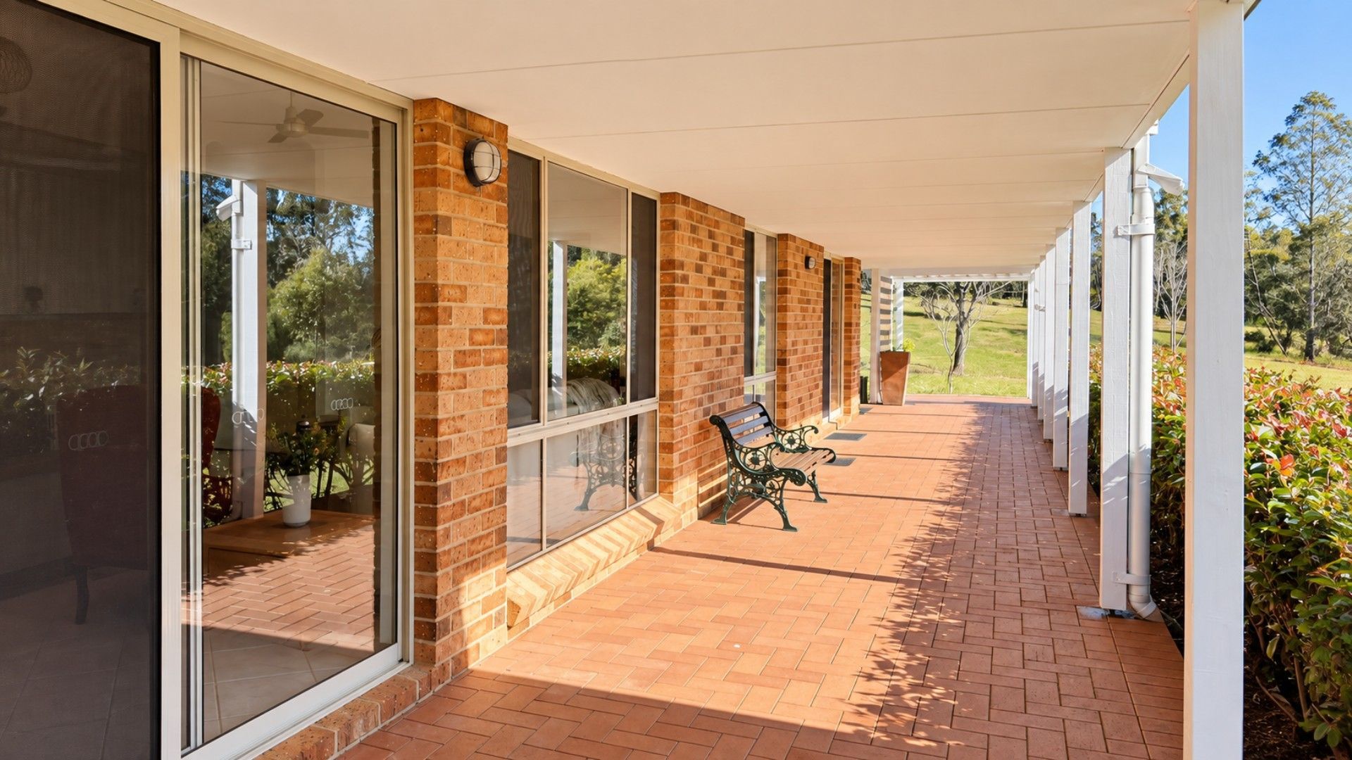 A covered outdoor area with a brick wall, large windows, a bench, and a view of the outdoors.