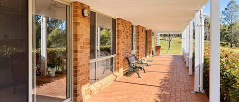 A covered outdoor area with a brick wall, large windows, a bench, and a view of the outdoors.