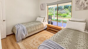 A bedroom with two single beds, a bench, a window with a view of a garden, and a door.