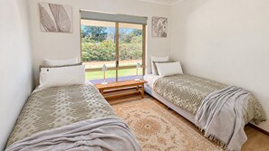 A bedroom with two single beds, a wooden bench, and a large window with a view of greenery.