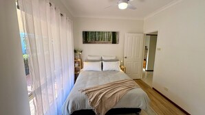 Un dormitorio con cama, mesita de noche, lámpara, un cuadro en la pared y una puerta que da a otra habitación.
