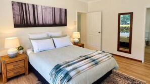 A bedroom with a bed, two bedside tables, a nightstand, a large mirror, and a painting of a forest.