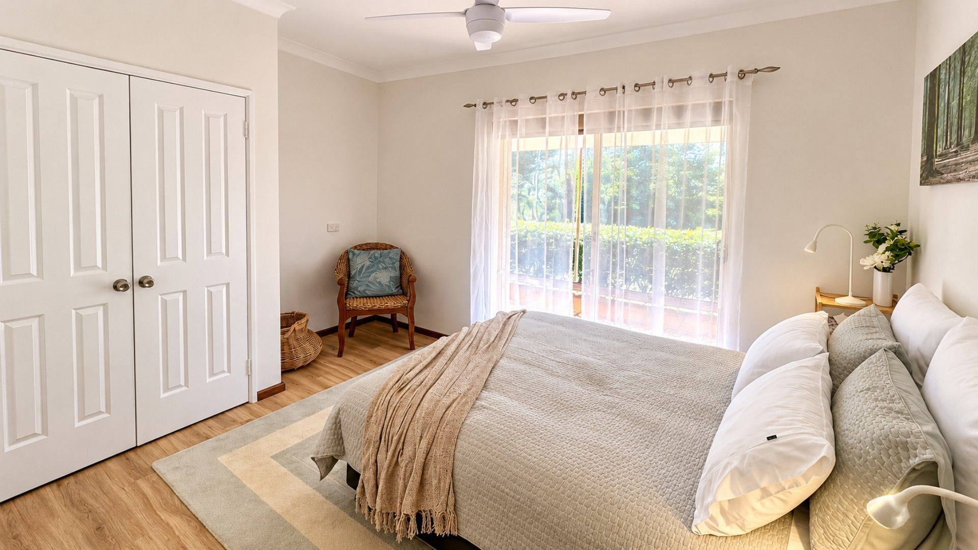 Un dormitorio con cama, una silla, un ventanal con cortinas y una puerta.