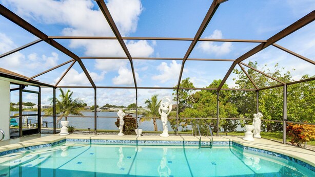 Ein Schwimmbad mit Glasveranda, umgeben von Statuen und Blick auf einen See.