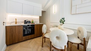 Una cocina moderna con armarios de madera, lavavajillas negro y encimera de mármol. Hay una mesa de comedor con sillas y un jarrón con una planta.