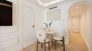 A hallway with a round table and two chairs, a potted plant, and a framed artwork on the wall.