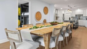 Un comedor moderno con una mesa y sillas de madera, una cocina al fondo y decoración en la pared.