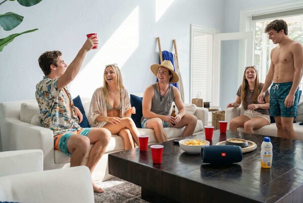 A group of people sitting on a white couch in a room with a large window, a coffee table with snacks, and a relaxed atmosphere.