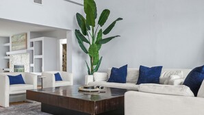 Una sala moderna con una planta grande, sofás blancos con cojines azules y una mesa de centro oscura.