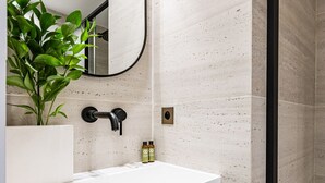 A modern bathroom with a white sink, a mirror, and a potted plant.