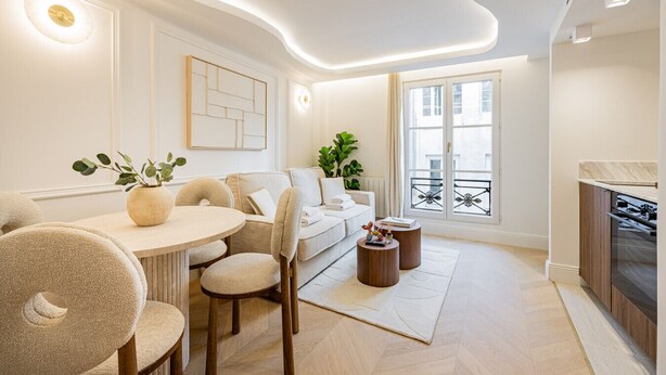 A modern living room with a round dining table, beige sofas, and a kitchen area with a stove.