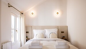 A hotel room with a large bed, two bedside tables, a window with curtains, and two wall-mounted lights.