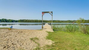 A wooden pier leading to a dock with a 'No Fishing' sign, surrounded by a sandy beach and grassy areas. - Walk to Cranberry Lake: Quaint Family Cottage (Oakland Township)