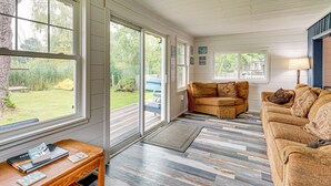 A spacious living room with a large window, a wooden coffee table, and a beige sofa. - Walk to Cranberry Lake: Quaint Family Cottage (Oakland Township)