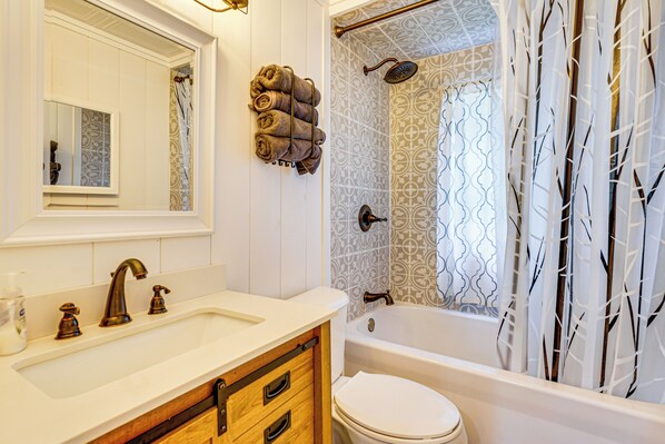 Een badkamer met een witte wastafel, een spiegel, een handdoekhouder, een bad en een toilet.
