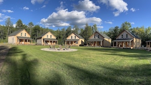 A row of wooden cabins with a circular seating area in the center. - The Cabins at Timber Ridge - #6 - Brand new cabins nestled in the woods of NH (Tamworth)